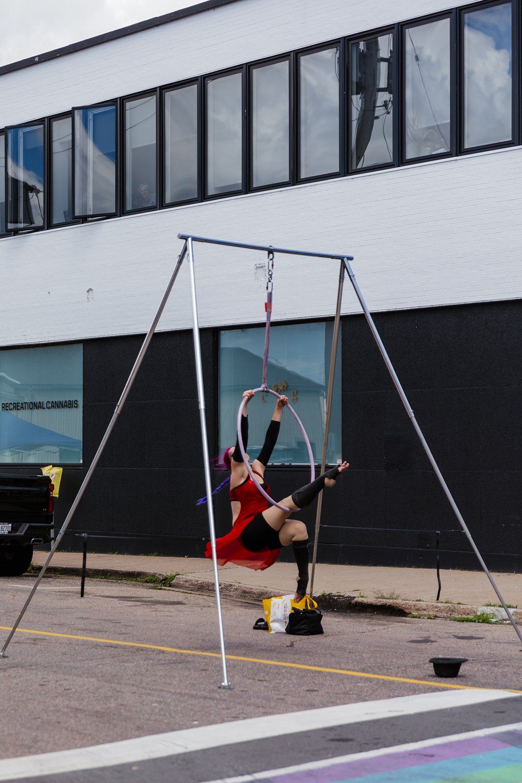 An aerialist in red performing on a hoop rigged from a free-standing frame in the street.