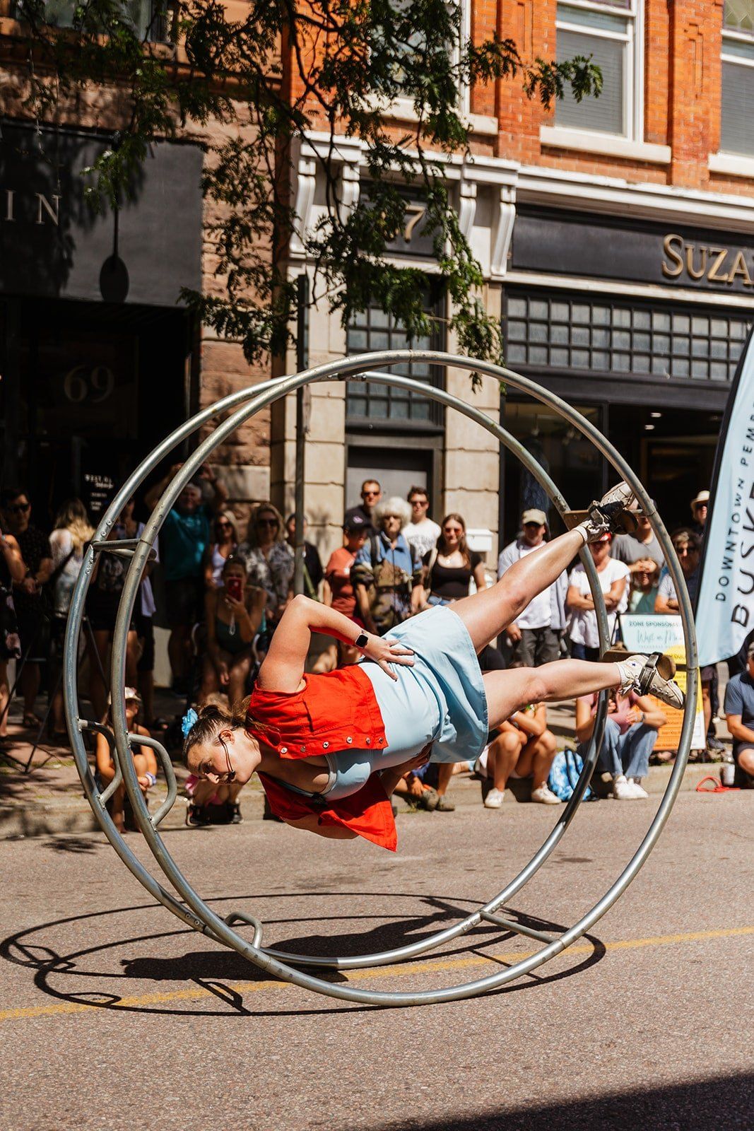 A performer spinning inside a cyr wheel on the street as onlookers watch.