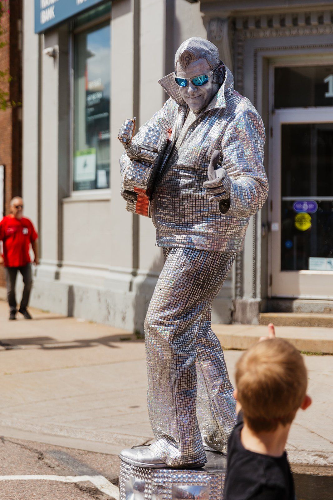 A living statue in silver costume standing motionless as a child looks up.