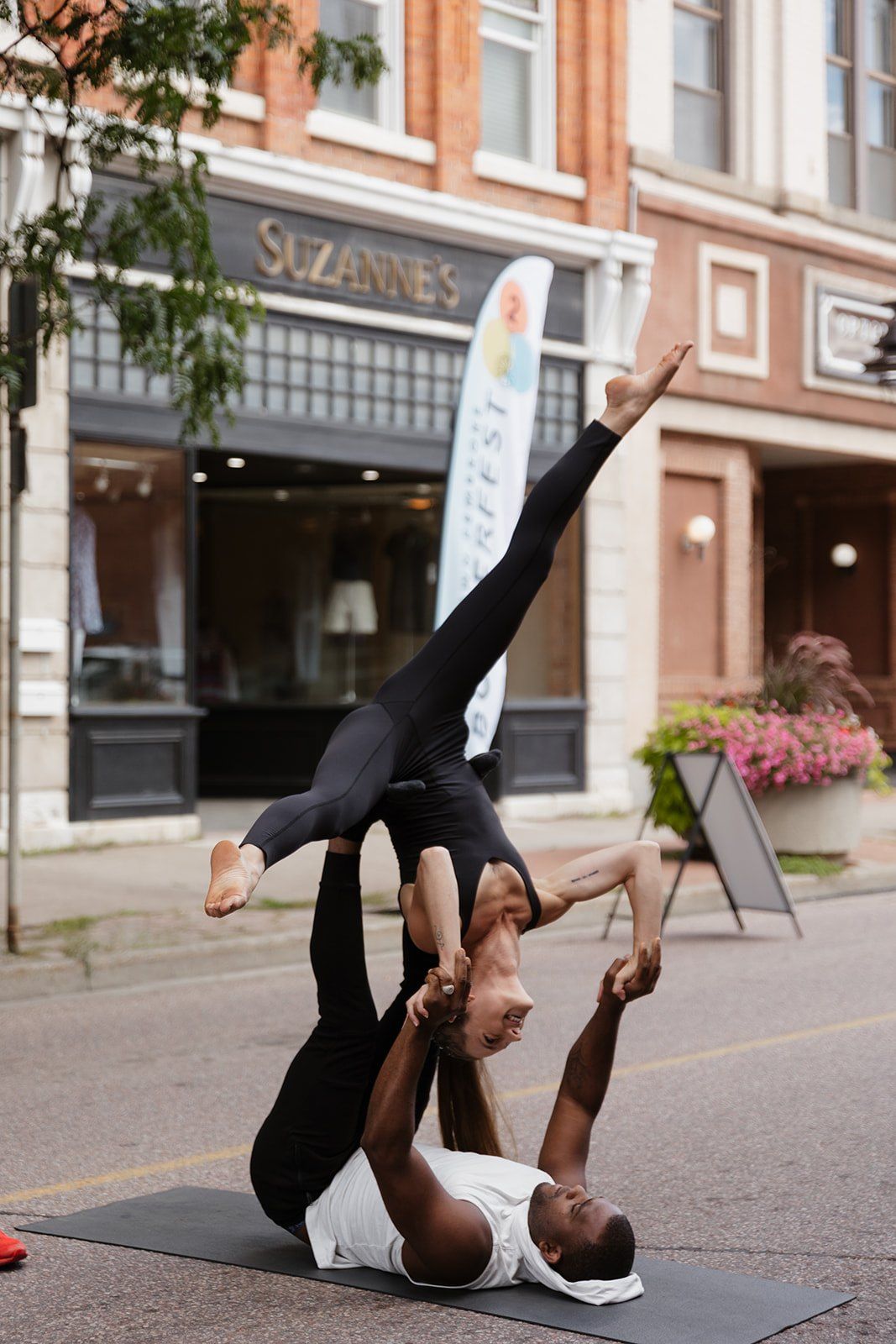 Two acrobats holding a partner balance on a mat in front of the shopfronts.