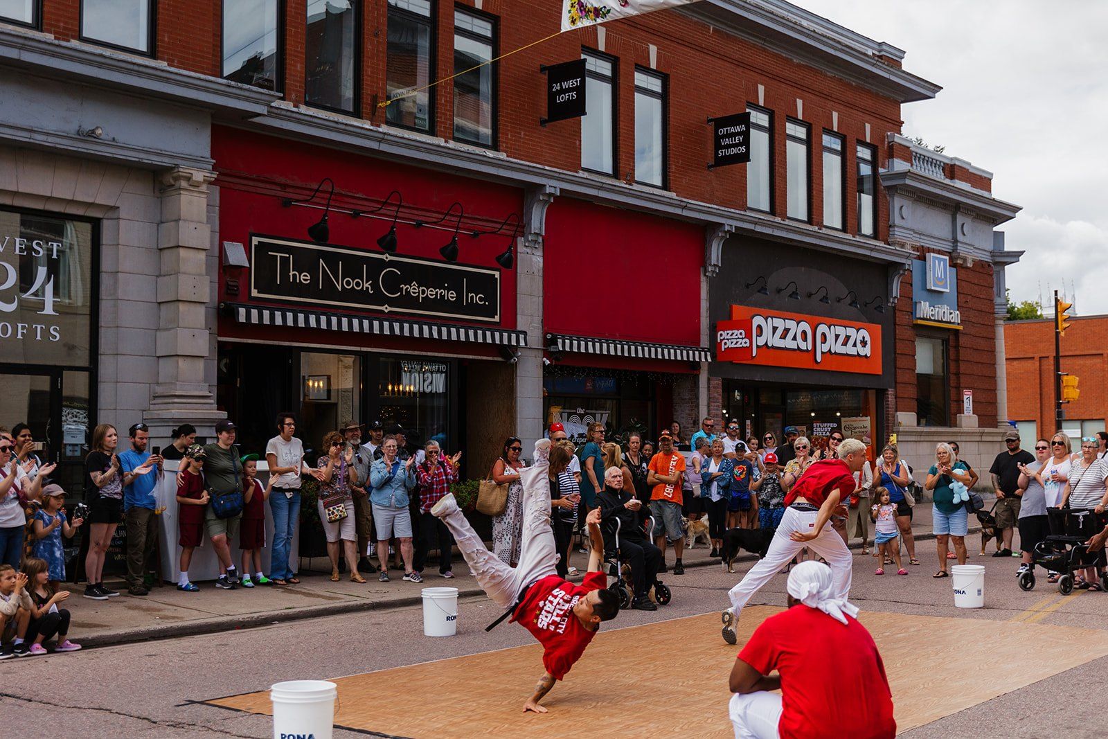 A performer mid-handstand on the road in front of a large crowd lining both sides of the street.